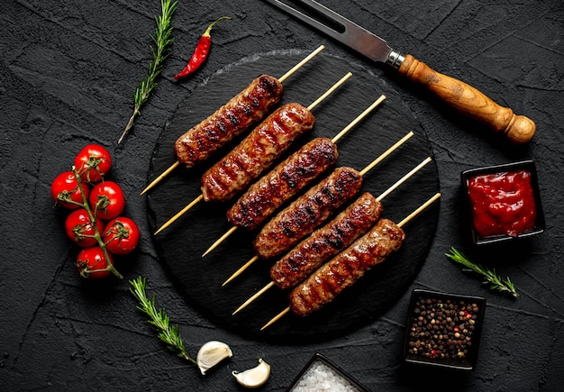 A black stone table with a plate of kebabs on it and a knife with spices on it.