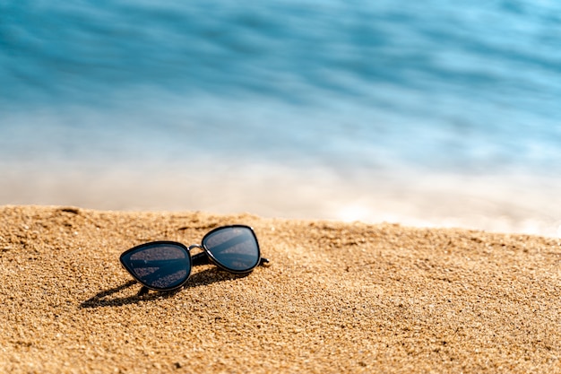 Black sunglasses on yellow sand and sea or ocen. Space for text or product. Summer vacation