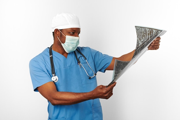 Black surgeon doctor man in blue coat white cap and surgeon mask holds x ray image white background