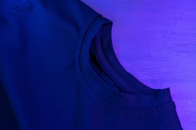 Black t-shirt in neon light close up on a table, copy space