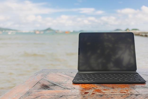 Black tablet with keyboard on table and sea view in concept of workation