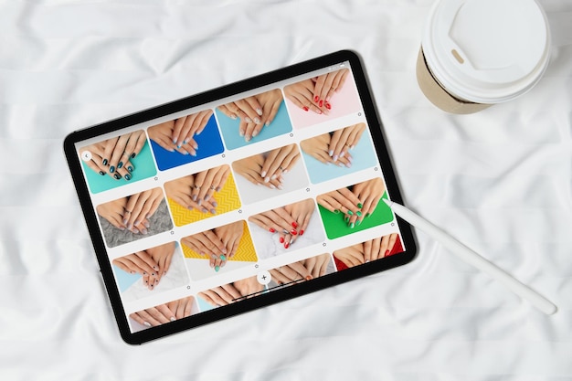 Black tablet with manicure designs on screen on white bed Beauty salon concept