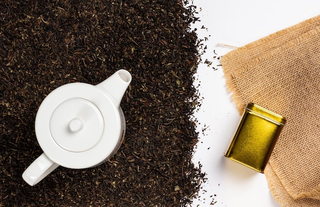 Black tea loose on white background with golden tea box on burlap and white teapot