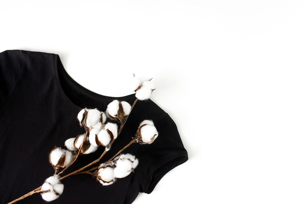 Photo black tshirt with cotton branch flat lay on white top view with copy space natural cotton fabric