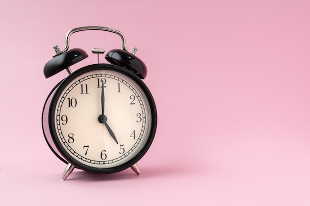 Black vintage alarm clock on a light pink background shows the time five hours