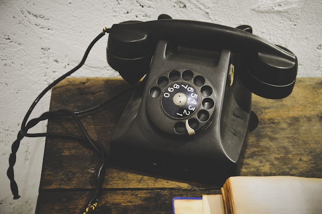 Black vintage telephone on wooden table and white grunge cement plaster wall