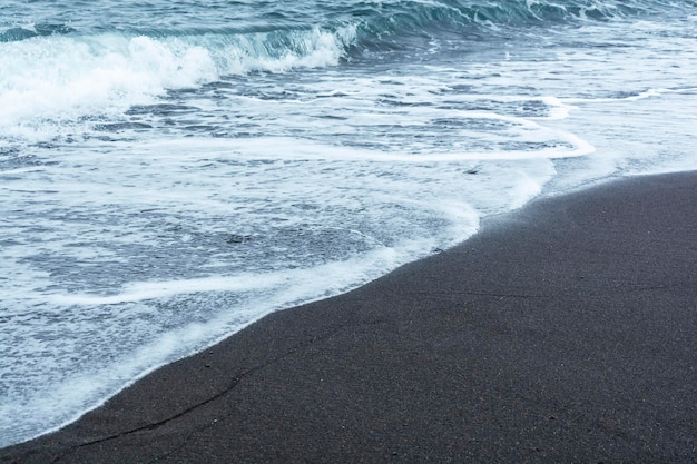 Black volcanic sand on the beach with waves