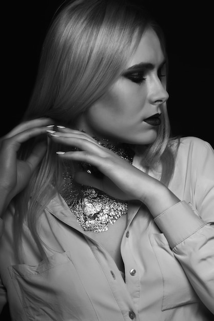 Black and white beauty shoot: glamor blond model posing at studio with bright makeup and foil on her neck