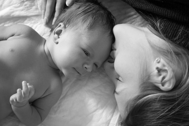 Black and white closeup portrait of young smiling mother lying with her 1 month old baby on bed