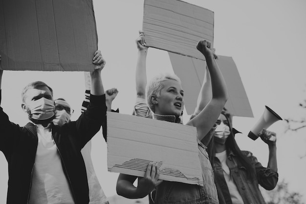 Black and white. Group of activists giving slogans in a rally. Caucasian men and women marching together in a protest in the city. Look angry, hopeful, confident. Blank banners for your design or ad.