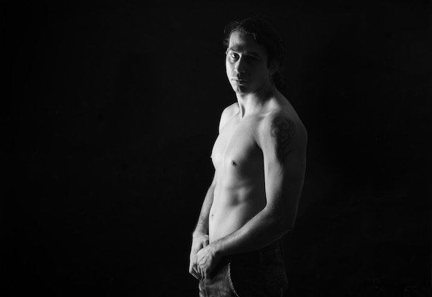 Black and white low key portrait of shirtless man looking at camera black background