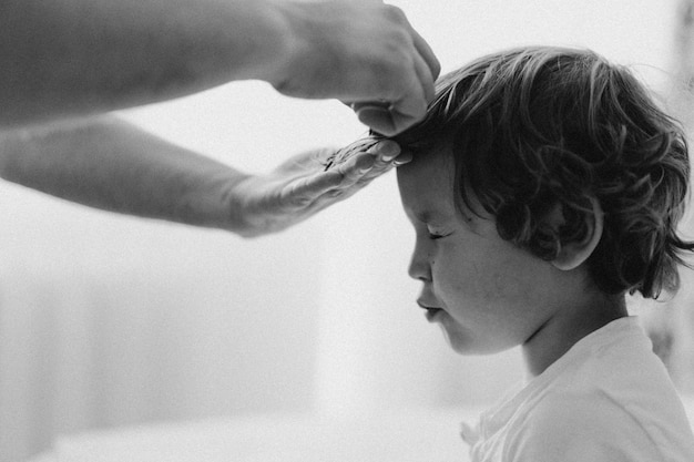 Black and white photo. Father cuts her son hair in the room