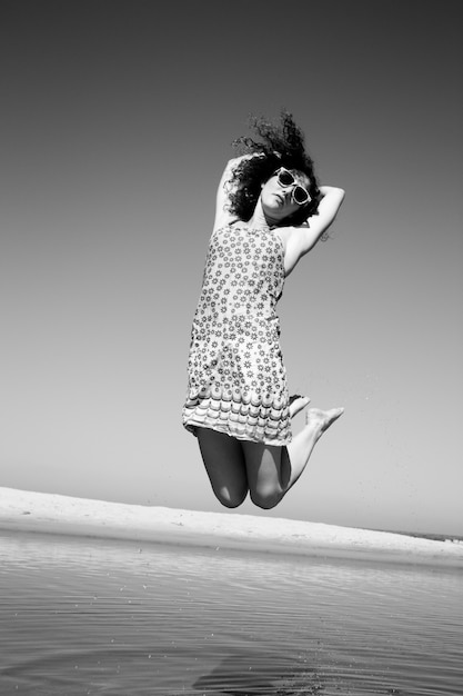 Black and white photo of a woman with curly dark hair jumping in a short sun dress