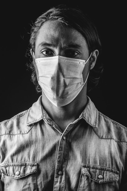 Black and white photography of a Latino ethnic man wearing a blue medical mask, wearing a blue shirt on a black background. Coronavirus concept. Coronavirus concept