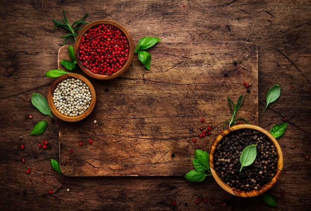 Black white and pink rose peppers in bowls assorted spices and spicy herbs on wooden rustic kitchen.