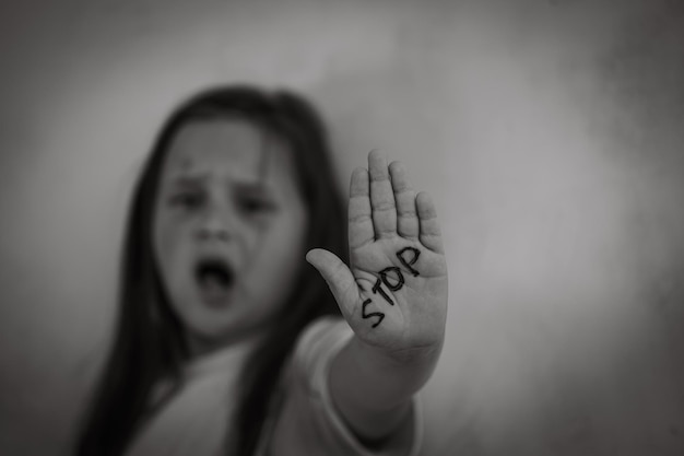 Black and white portrait of little afraid girl shouting stretching hand showing inscription stop on palm Soft focus