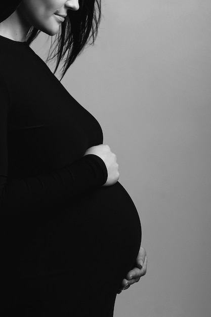 Photo black and white silhouette studio photo of pregnant woman in black dress holds her pregnant belly