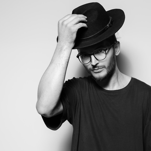 Black and white studio portrait of young attractive man wearing black hat