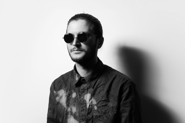 Black and white studio portrait of young handsome man with beard wearing shades