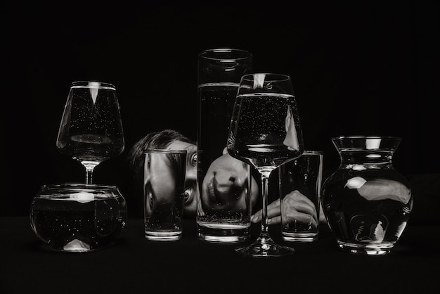 Black and white surreal portrait of a man looking through glasses of water on a black background