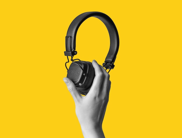 Black wireless headphones in hand on bright yellow background