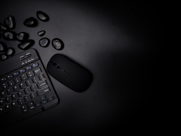 A black wireless keyboard and mouse with black stone on a black background