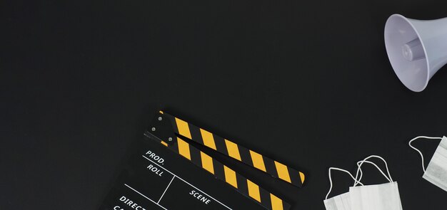 Black with yellow clapperboard or movie slate and face mask ,magaphone on black background.