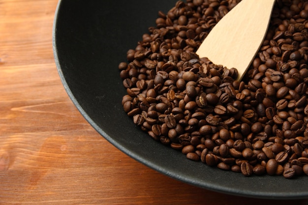 Black wok pan with coffee beans on wooden table close up