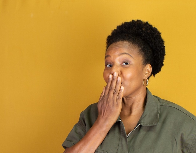 Black woman in green clothes making a gesture  on a yellow surface