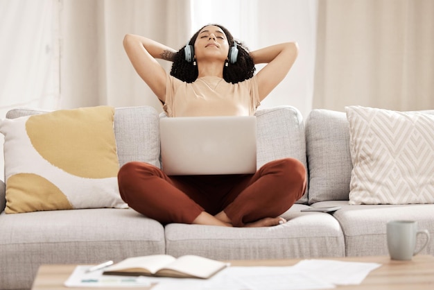 Black woman headphones and laptop to relax on couch for wellness and meditation in living room Young female girl and earphones for podcast rest and on break for health calm and peaceful on sofa