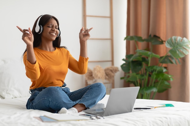 Black Woman Listening Music Using Laptop And Headphones In Bedroom