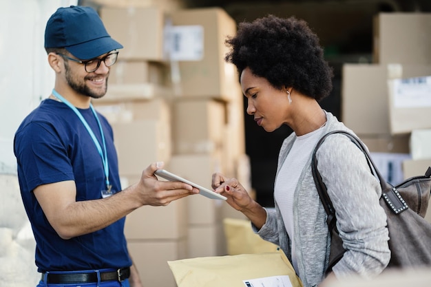 Black woman using digital tablet to sing a delivery form a courier