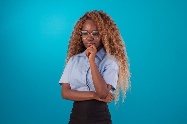 Black woman with curly hair in studio photo wearing blue shirt and black skirt and making various facial expressions.