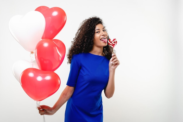 Black woman with heart shaped lollypop candy and colorful balloons isolated