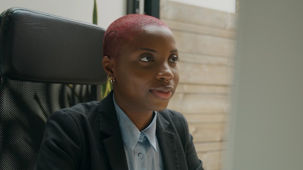 Black woman with pink hair sitting at her desk