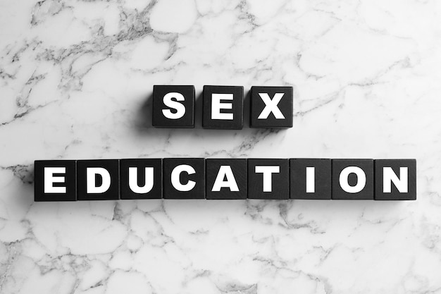 Photo black wooden blocks with phrase sex education on marble background flat lay