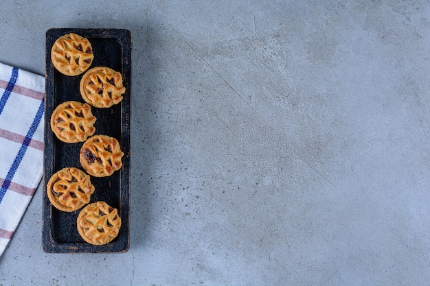 A black wooden board of round fruit biscuits on a stone background .