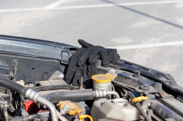 Black work gloves of a mechanic on the edge under an open hood of a flat-four (boxer) car engine compartment