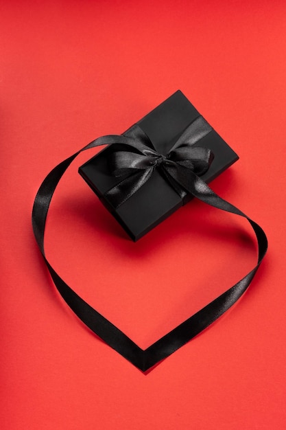 Black wrapped gift box with black bow and ribbon laid out as heart on red Copy space Vertical shot