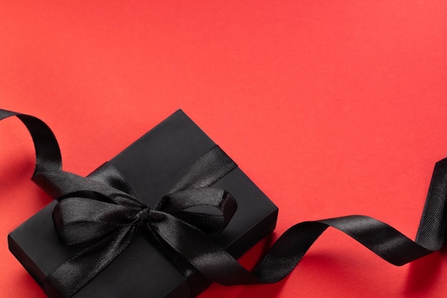 Black wrapped gift box with black ribbon and bow on red Minimal image for holiday shopping sales