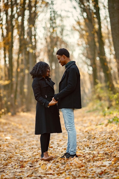 Black young man and his girlfriend holding hands. Romantic couple walking in autumn park. Man and woman wearing black coats.