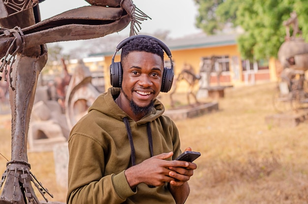 Black young man relaxing outdoors listening to music using phone and headphones Copy space