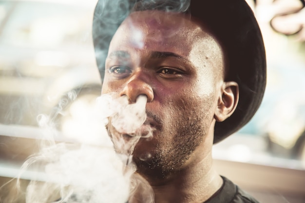 black young man with a hat blowing smoke from his mouth