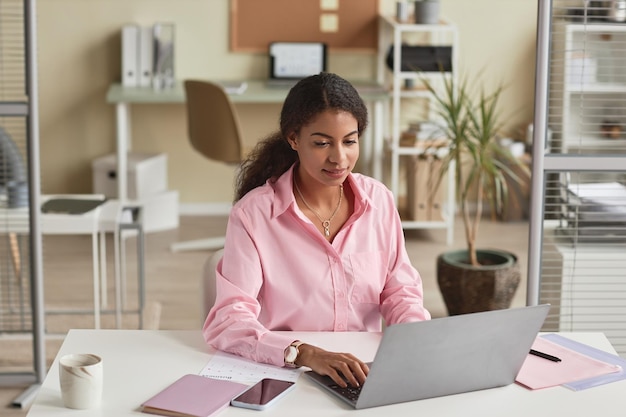 Black young woman wearing pink in office using computer