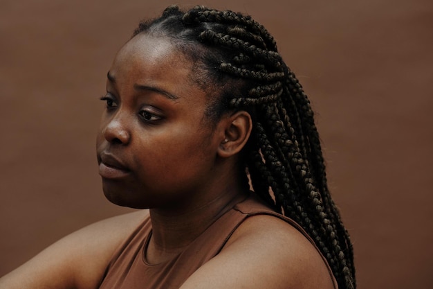 Black young woman with braids sitting with blank expression against the brown background