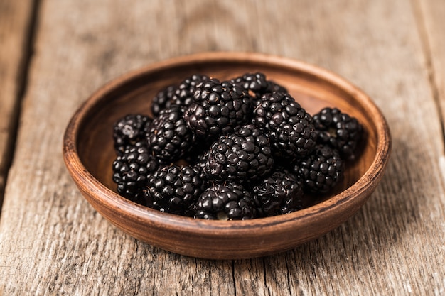 Blackberries in plate on wood background.