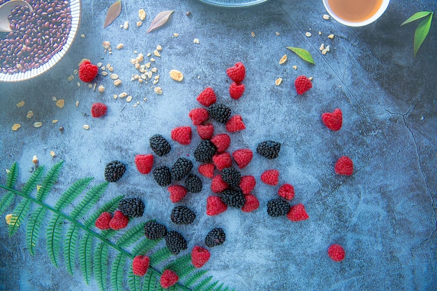 Photo blackberries and raspberries on a blue stone background with corn flakes around