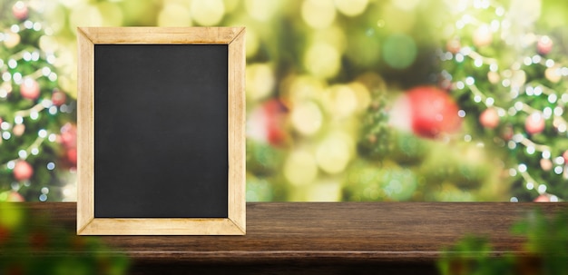 Blackboard on brown wood table top with blur christmas tree red decor ball