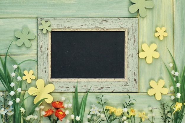 Blackboard framed with spring flowers on neutral background, copy-space