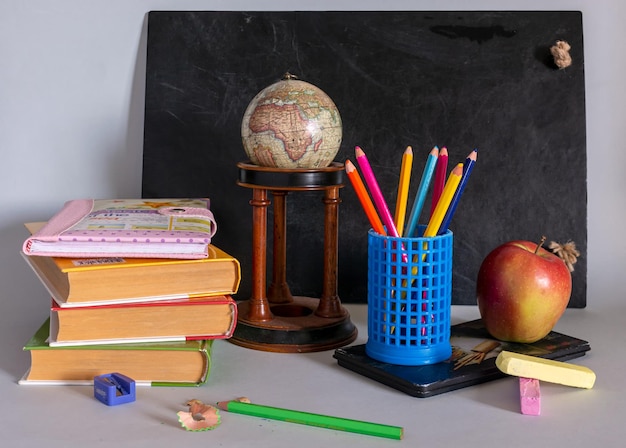 Blackboard, textbooks, notepads, pencils, a globe and an apple